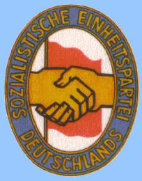 Emblem: Handschlag zwischen KPD und SPD vor der roten Fahne der Arbeiterklasse auf weiem Grund, Parteiname als Umschrift auf blauem Grund